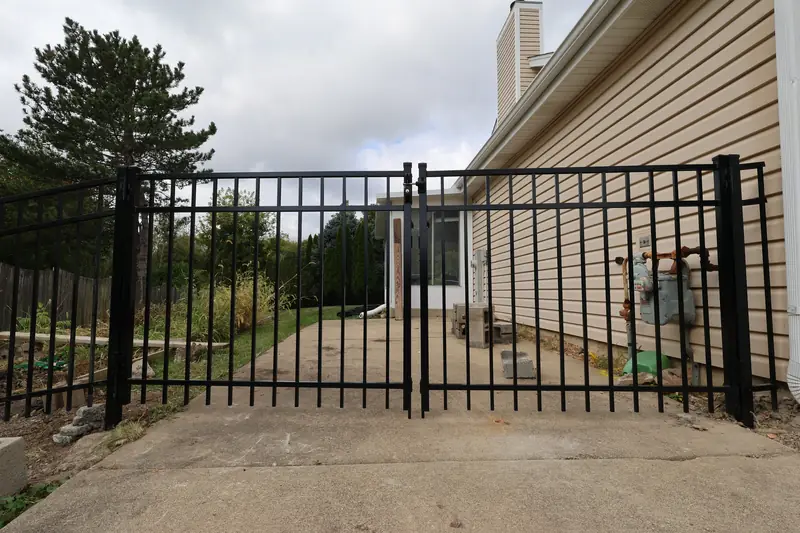 Black aluminum double swing gate across a concrete drive beside a house