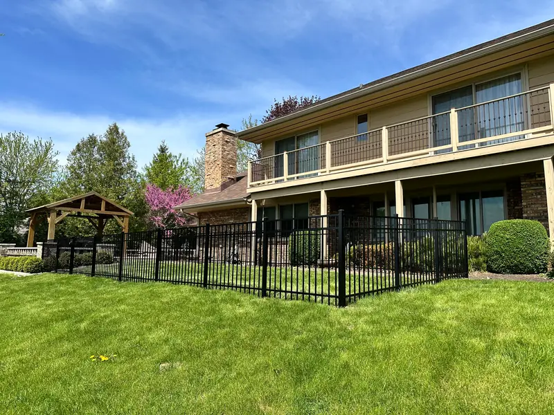Low black aluminum fence enclosing a backyard lawn and patio behind a two-story house