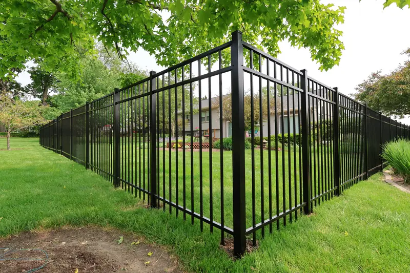 Black aluminum picket fence turning a corner around a grassy backyard