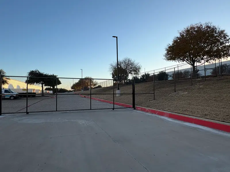 8 ft black vinyl-coated chain link fence with a wide vehicle gate at a commercial lot