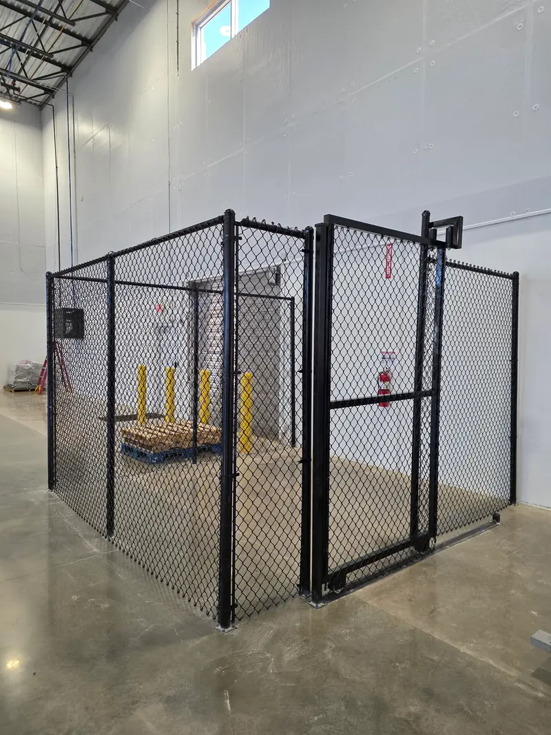 Black chain link security enclosure with a locking gate inside a warehouse