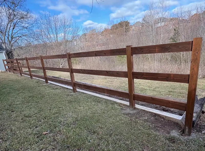 Four-foot three-rail stained wood ranch fence along an open field