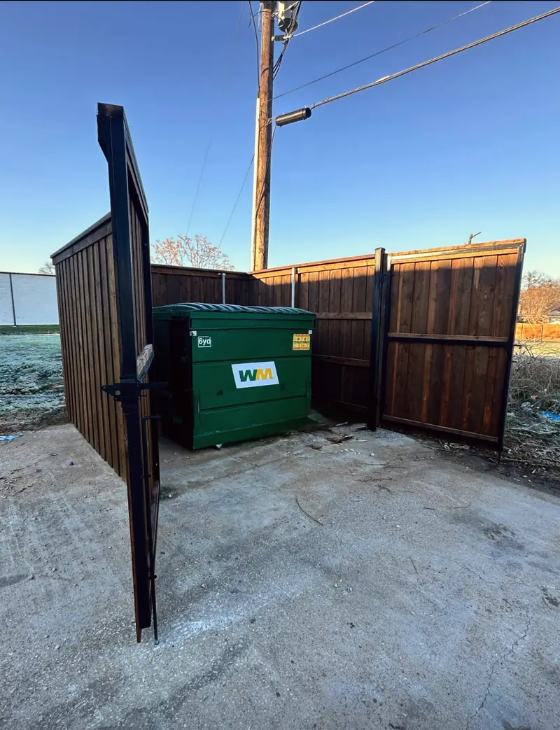 Stained wood dumpster enclosure with black steel-framed swing gates
