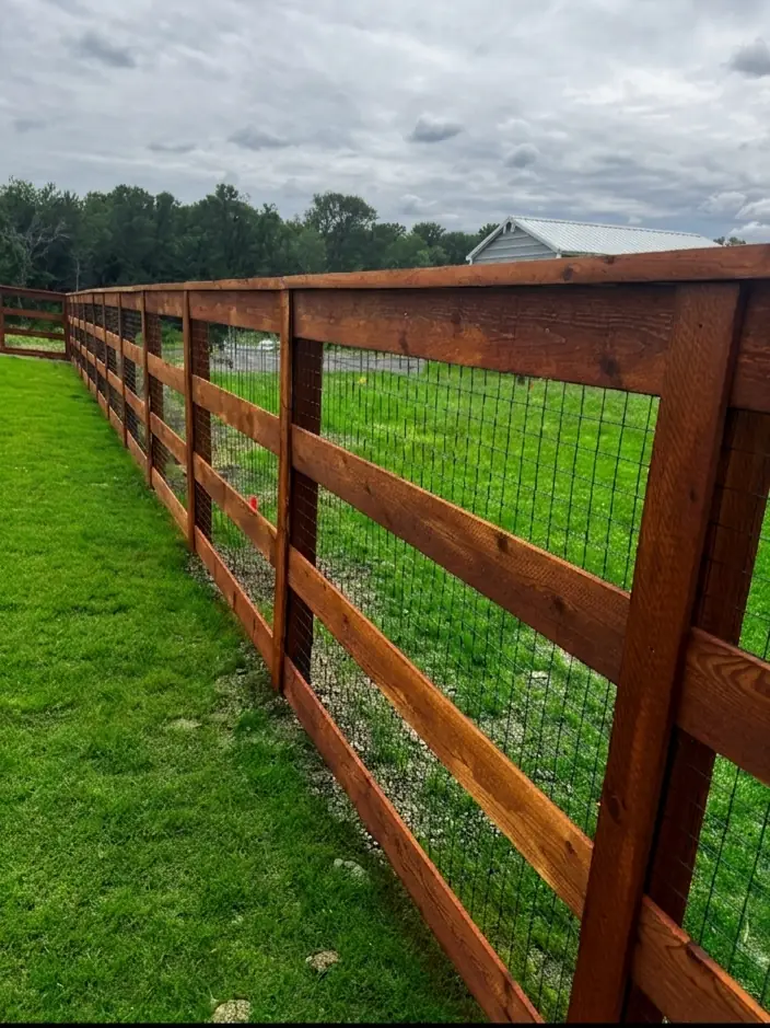 Wood rail fence backed with welded wire mesh along a grassy pasture